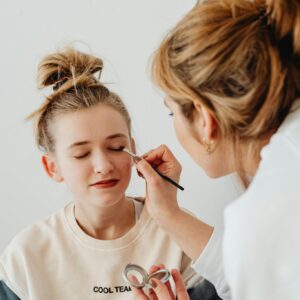 A makeup artist skillfully applies eyeshadow on a teenager with a relaxed expression.